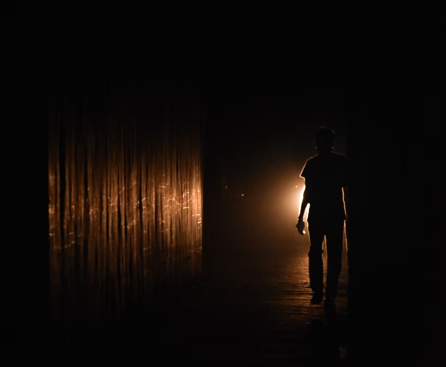 A lone figure walking down a dark passageway toward a distant light.